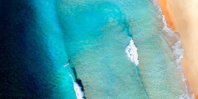 Aerial shot of a surfer paddling in the ocean