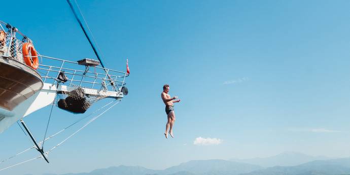 Man jumping off a yacht into blue water