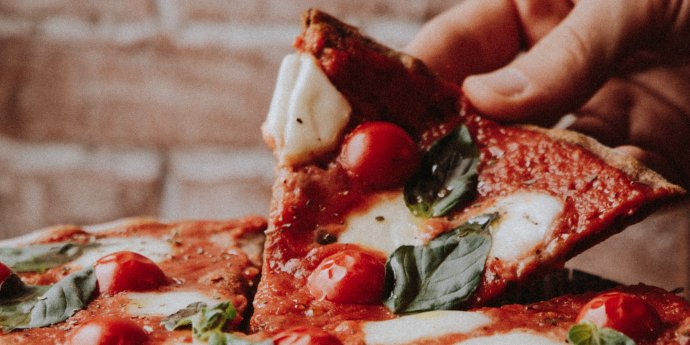 person's hand holding slice of pizza