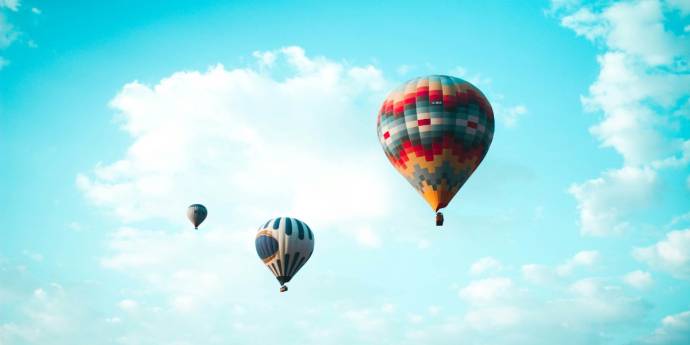 Three hot air balloons drifting in a light blue sky with soft clouds